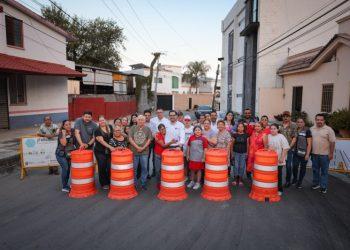 Group of diverse people posing behind orange construction barrels on a street for a community event/initiative.